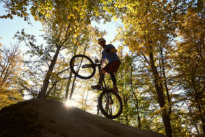 mountain biking cyclist balancing on back wheel on boulder in sunny forest
