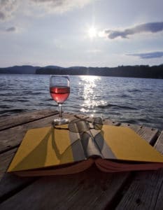 Glass of red wine, book, and sunglasses on dock at lake in the Lakes Region NH